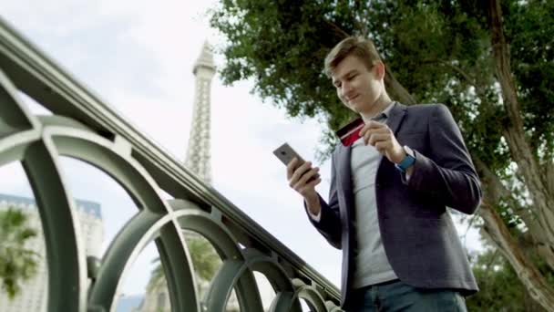 Молодой человек делает покупки онлайн с Эйфелевой башней на заднем плане — стоковое видео