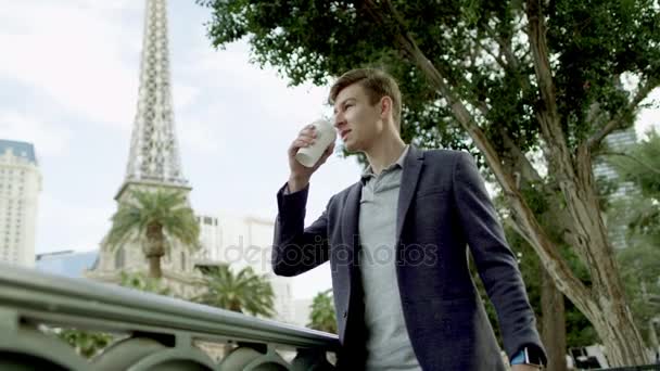 Giovane uomo sta bevendo caffè mentre in piedi su una strada con la torre Eiffel su uno sfondo — Video Stock