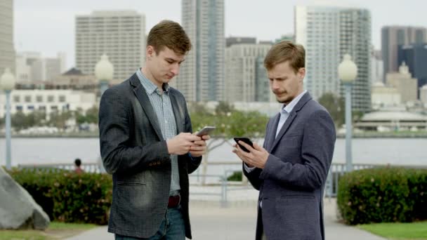 Δύο επιχειρηματίες στέκονται σε μια οδό με smartphones τους — Αρχείο Βίντεο