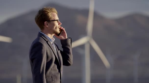 Человек разговаривает с телефоном возле ветряных мельниц — стоковое видео