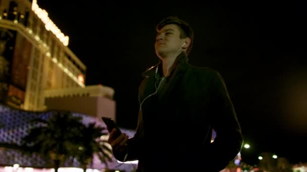 Young joyful man is listening to music on a sidewalk at night — Stock Video