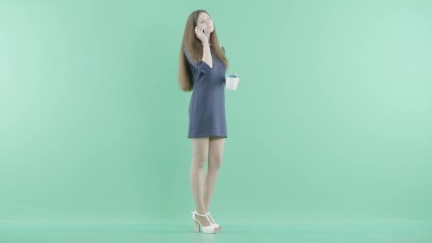 Una chica descontenta tiene una conversación telefónica bebiendo de una taza — Vídeos de Stock