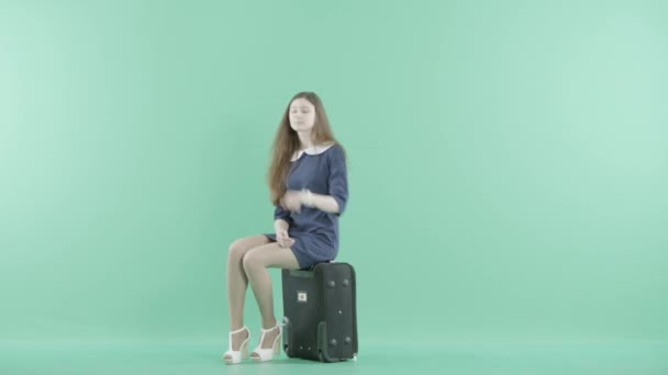 Una buena chica en vestido se sienta en la maleta — Vídeo de stock