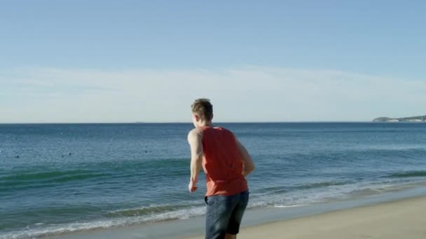 Молодой спортсмен бежит к океану туда-сюда — стоковое видео