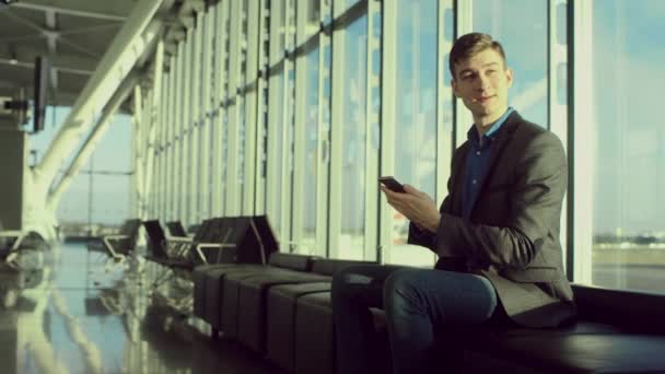 Молодой бизнесмен разговаривает за своим смартфоном в аэропорту — стоковое видео