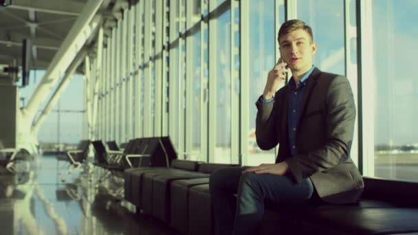 Joven hombre de negocios está teniendo una conversación telefónica mientras espera su vuelo — Vídeo de stock