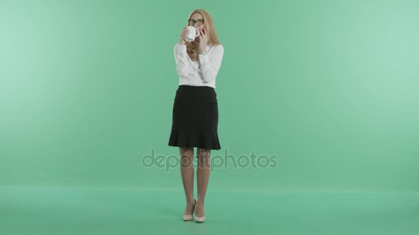 Een lachende jonge vrouw drinken thee en gesprekken over de telefoon — Stockvideo