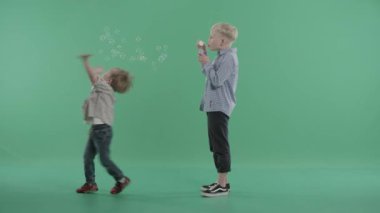 Yeşil arka plana karşı iki kardeş sabun köpüğü ile oynamak