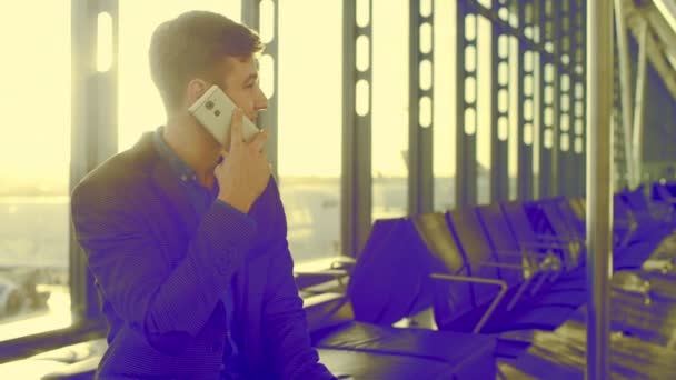 Молодой человек разговаривает по телефону со своим смартфоном в аэропорту — стоковое видео