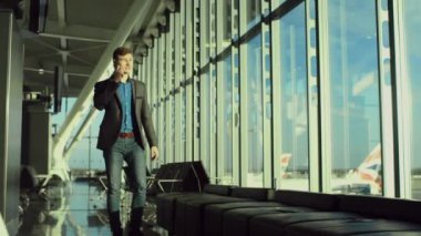 Genç adam onun smartphone bir Havalimanı pencere yakınındaki üzerinde konuşuyor