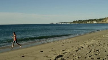 Genç atlet sevinçle güneşli sahil üzerinde çalışıyor