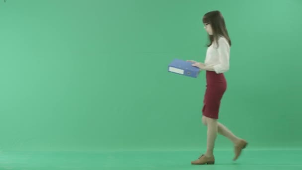 Joven mujer de negocios se detiene a echar un vistazo a una carpeta azul que sostiene — Vídeos de Stock