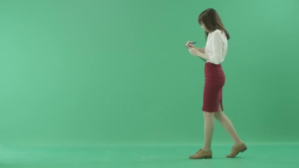 Młoda kobieta idzie z schowka, mówiąc na telefon komórkowy i dokonywanie notatek — Wideo stockowe