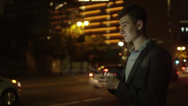 Jovem estudante está enviando mensagens enquanto está de pé em uma rua à noite — Vídeo de Stock