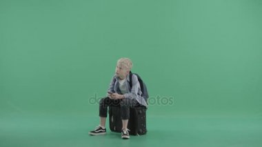 Bir akıllı telefon elinde bavulla oturan genç çocuk