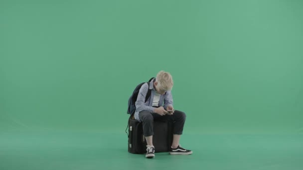 Szőke fiú ül, vár egy bőrönd — Stock videók