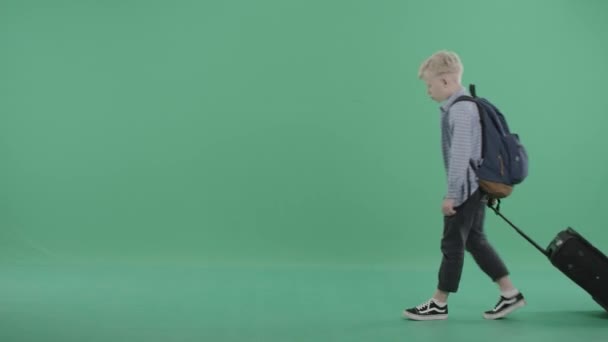 Caucasiano menino rodas uma mala na tela verde — Vídeo de Stock