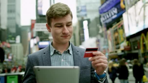 若い男が彼のタブレット pc とカードを使用して、タイムズ ・ スクエアのオンライン ショッピング — ストック動画