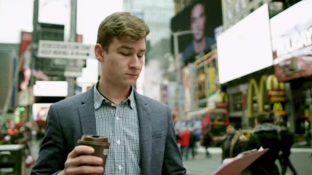 O jovem está a escrever algo no seu mapa enquanto bebe café na Times Square. — Vídeo de Stock