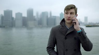 Genç yakışıklı turist Hudson Nehri yakınında smartphone üzerinde konuşuyor