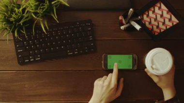 Yukarıdan aşağı onun akıllı telefon Yeşil perde-in kahve yudumlarken swiping adam vurdu