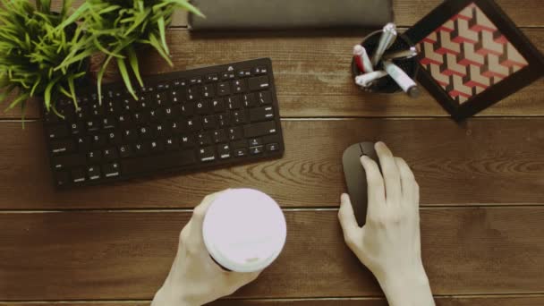 トップダウンの一方でのコーヒーのカップを持つコンピューターのマウスを使用している人のショット — ストック動画
