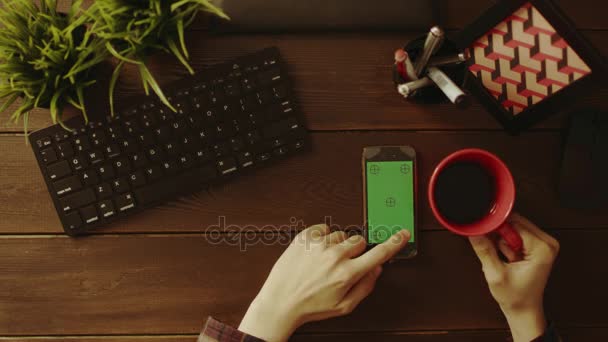 Вид сверху на человека с помощью смартфона с зеленым экраном и питьевым чаем — стоковое видео