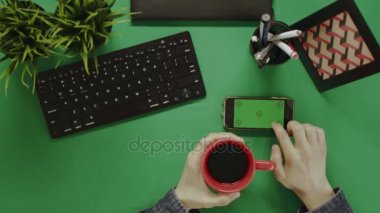 Yukarıdan aşağıya smartphone yeşil ekran swiping ve kahve içme erkek el görünümünü
