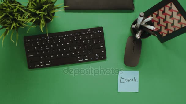 Blick von oben auf einen Mann, der Zettel mit der Aufschrift "Kaffeepause" darauf klebt und eine Tasse Kaffee dazwischen auf einen grünen Tisch legt — Stockvideo