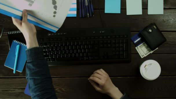 Un homme s'assoit au clavier et prend le dossier et vérifie les informations . — Video