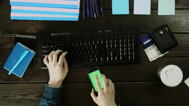 Muž, psaní na klávesnici a používá svůj telefon. — Stock video