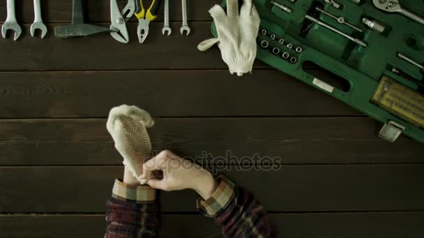 Мужчина сидит за столом возле ящика с инструментами, надевает перчатки и разминает руки — стоковое видео