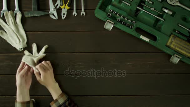 En man sitter vid ett bord nära verktygslådan och sätter på handskar och tar bort dem. — Stockvideo