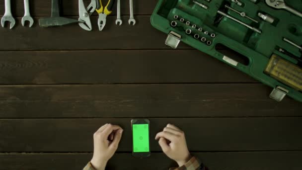 Egy férfi ül egy asztal mellett toolbox, és használja a telefon. — Stock videók