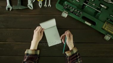 Bir adam araçları yakınındaki bir masada oturur vardır ve bu bir defterde yazmak düşünüyor.