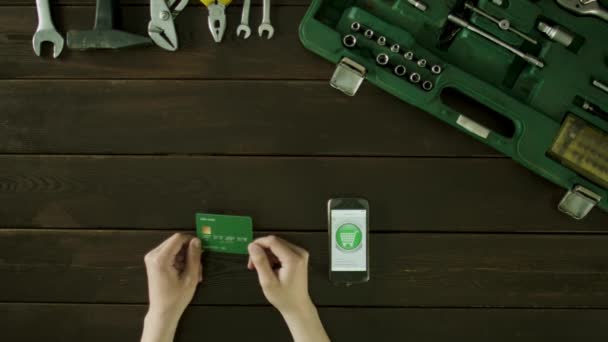 A man sits at a table beside him is a suitcase with the tools and he is getting to buy something in the internet using a bank card. — Stock Video