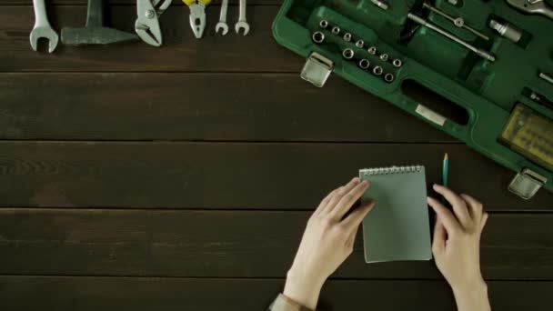 Ένας άνδρας κάθεται σε ένα τραπέζι κοντά τα εργαλεία είναι και σκέφτεται ότι για να γράψετε σε ένα σημειωματάριο. — Αρχείο Βίντεο