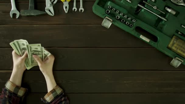 En man sitter vid ett bord nära verktygen är och och räknar pengar. — Stockvideo