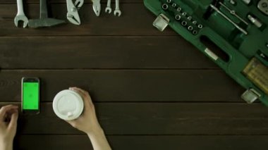 Bir adam araç kutusu yakınındaki bir masada oturur ve kahve içer ve telefonda bir şey izlemek.