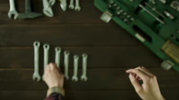 Ένας άνδρας κάθεται σε ένα τραπέζι κοντά τα εργαλεία και καθορίζει τα κλειδιά σε μέγεθος και διπλώνει πίσω. — Αρχείο Βίντεο