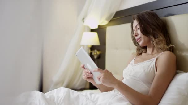 Młoda piękna kobieta za pomocą cyfrowego tabletu leżąc w łóżku — Wideo stockowe