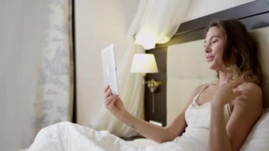Genç kadın yatakta yatarken onun tablet PC'de görüntülü sohbet sahip