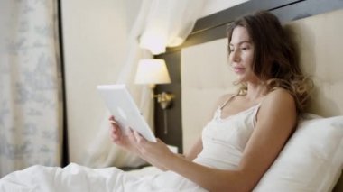 Neşeli kadın yatakta yatarken onun tablet PC'de video çeviri yapıyor