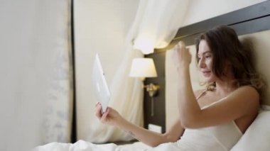 Kadın yatakta yatıyor ve onun dijital tablet görüntülü sohbet başlamadan önce saçlarını düzeltir