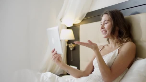 Mulher alegre deitada na cama e tendo um bate-papo por vídeo em seu tablet digital — Vídeo de Stock