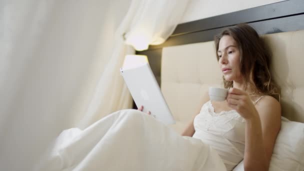 Kvinna med hjälp av TabletPC i sängen när man dricker kaffe — Stockvideo