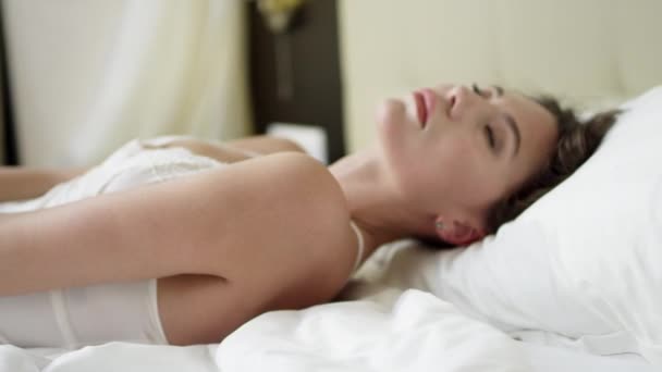 Женщина соблазнительно гладит себя, лежа на кровати, одетая во сне. — стоковое видео