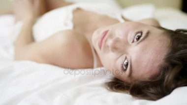 Genç çekici kadın yatakta onun arkasında yatan beyaz pijama gömlek pozsyonda poz