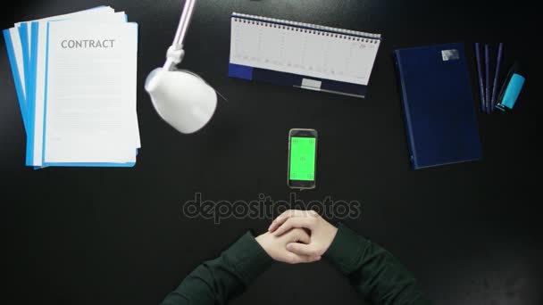 Een man is aan een bureau zitten en met behulp van een telefoon. — Stockvideo