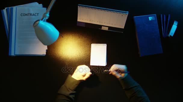 Een man is aan een bureau zitten en met behulp van een telefoon. — Stockvideo